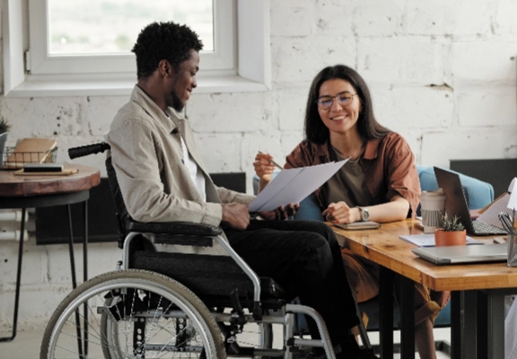 a man in a wheelchair reading with a helper